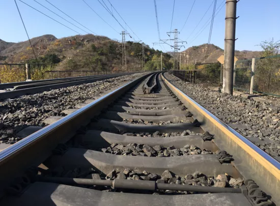 Eisenbahnstrecke biegt rechts ab, Schotterbett, Oberleitung, Bäume und Berge.